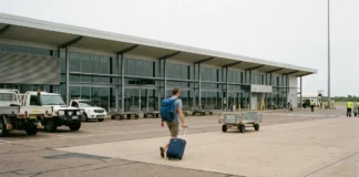 Letiště Darwin (DRW): doprava, aerolinky a tipy Terminální budova letišti Darwin s cestujícím nesoucím kufr a batoh přicházejícím k vchodu